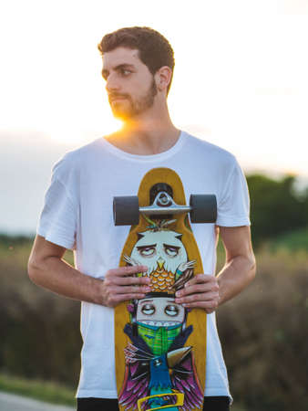 A vertical shot of a man holding a skateboard during the sunsetの写真素材