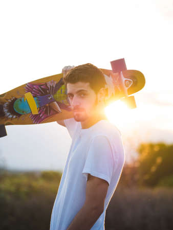A vertical shot of a man holding a skateboard during the sunsetの写真素材