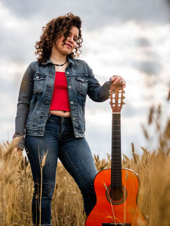 A shallow focus shot of a beautiful young female playing guitar in a wheat fieldの写真素材