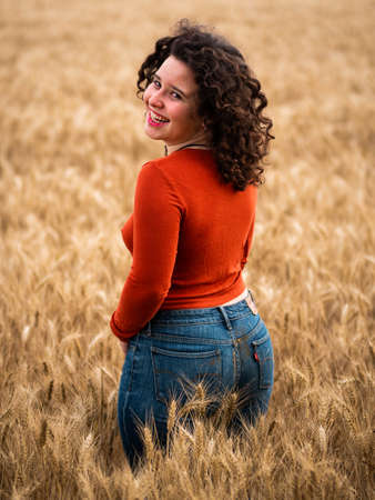 A shallow focus shot of a beautiful attractive female posing at camera in the wheat fieldの写真素材