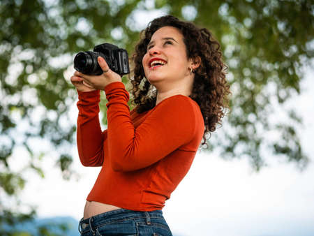 A curly Caucasian woman holding a camera during an outdoors shooting