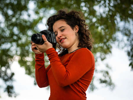 A curly Caucasian woman holding a camera during an outdoors shootingの写真素材