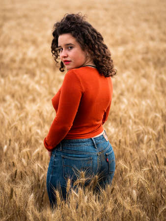 A shallow focus shot of a beautiful attractive female posing at camera in the wheat fieldの写真素材