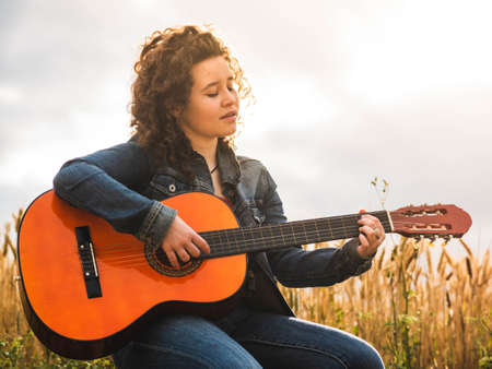 A shallow focus shot of a beautiful young female playing guitar in a wheat fieldの写真素材