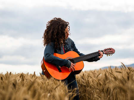 A shallow focus shot of a beautiful young female playing guitar in a wheat fieldの写真素材