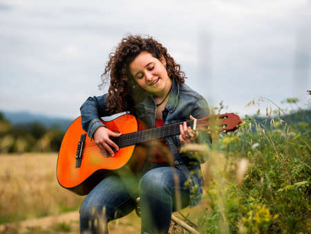 A shallow focus shot of a beautiful young female playing guitar in a wheat fieldの写真素材