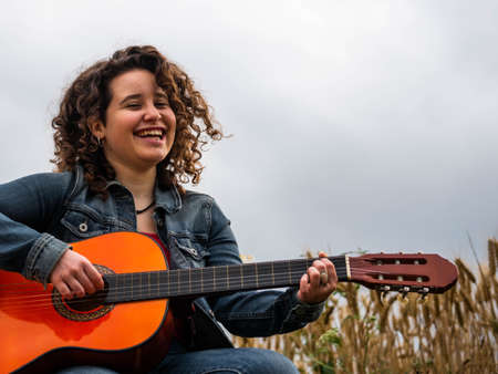 A shallow focus shot of a beautiful young female playing guitar in a wheat fieldの写真素材