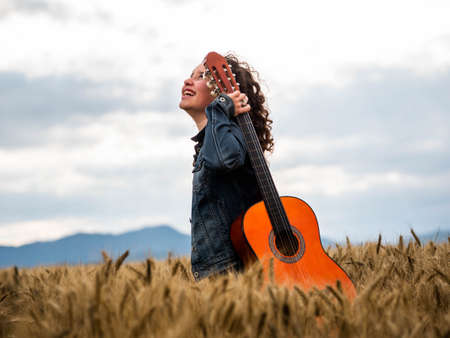 A shallow focus shot of a beautiful young female playing guitar in a wheat fieldの写真素材