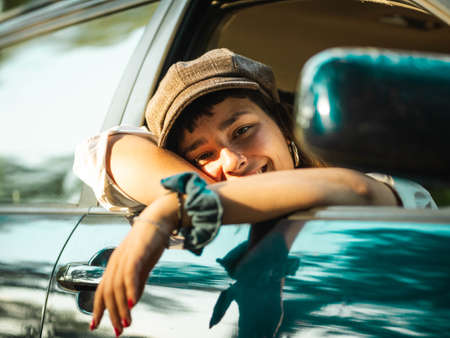 A picture of a brunette female in a black car under the sunlight