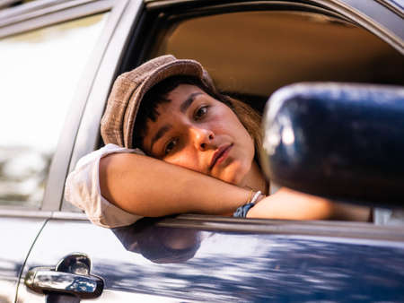 A picture of a brunette female in a black car under the sunlight