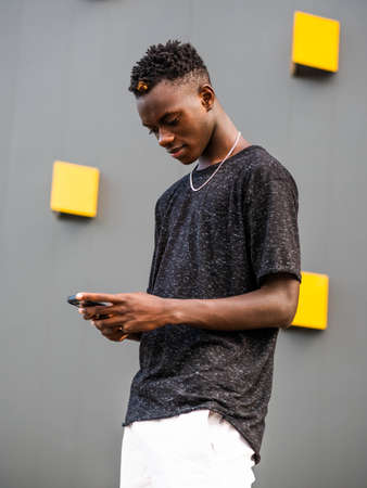 young black male on a gray wall background with phoneの写真素材