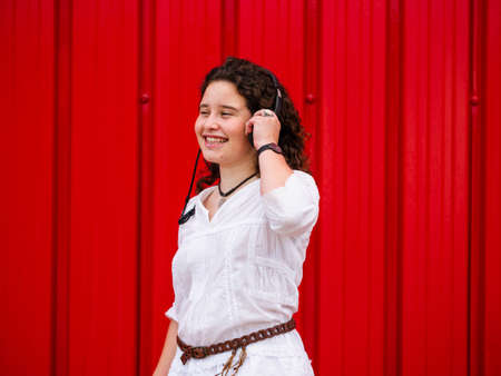 A young Caucasian woman happily listening to musing with headphones near a red wallの写真素材