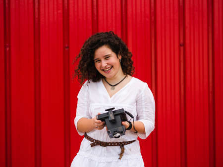 A young attractive female with an old professional photo camera against a red backgroundの写真素材