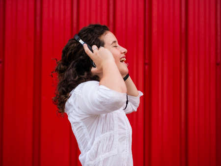 A young Caucasian woman happily listening to musing with headphones near a red wallの写真素材
