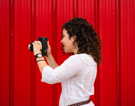 A young attractive female with an old professional photo camera against a red backgroundの写真素材