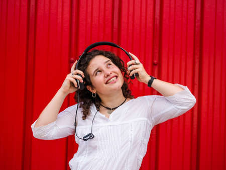A young Caucasian woman happily listening to musing with headphones near a red wallの写真素材