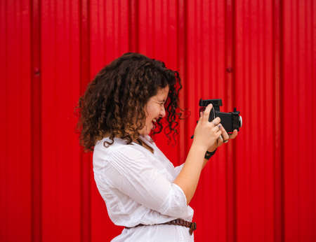 A young attractive female with an old professional photo camera against a red backgroundの写真素材