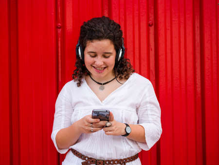 A young Caucasian woman happily listening to musing with headphones near a red wallの写真素材