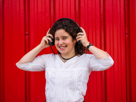 A young Caucasian woman happily listening to musing with headphones near a red wallの写真素材