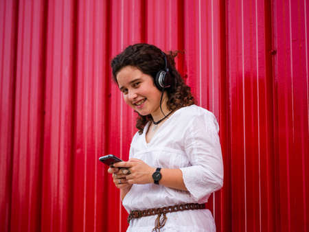 A young Caucasian woman happily listening to musing with headphones near a red wallの写真素材