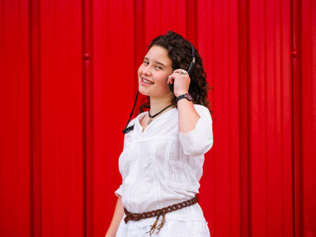 A young Caucasian woman happily listening to musing with headphones near a red wallの写真素材