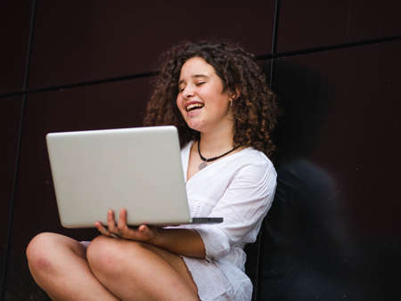 A Caucasian woman with curly hair holding a laptop