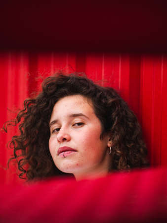 A shallow focus shot of a Caucasian female with curly hair on red backgroundの写真素材