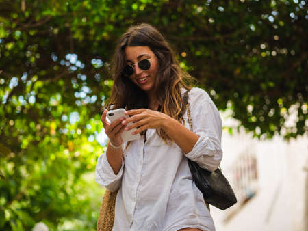 beautiful attractive female taking a selfie with her smartphone. Tourist taking selfie in a street surrounded by trees. Woman taking selfie standing at the beachの写真素材