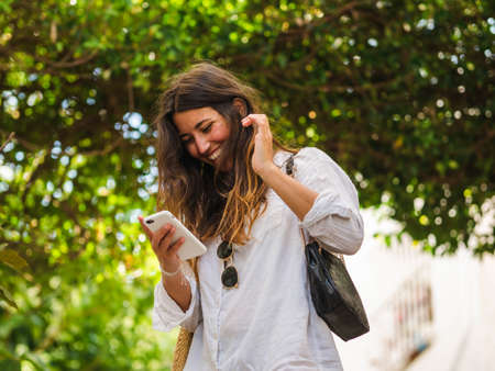 beautiful attractive female taking a selfie with her smartphone. Tourist taking selfie in a street surrounded by trees. Woman taking selfie standing at the beachの写真素材