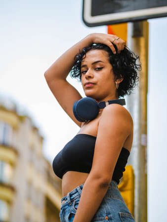 Brazilian woman with headphones in the street. woman sitting on the roof with a modern building in the backgroundの写真素材