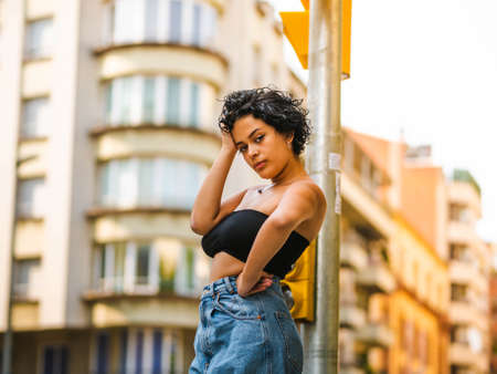Brazilian woman with headphones in the street. woman sitting on the roof with a modern building in the backgroundの写真素材