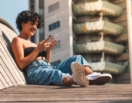 Brazilian woman with headphones in the street. woman sitting on the roof with a modern building in the backgroundの写真素材