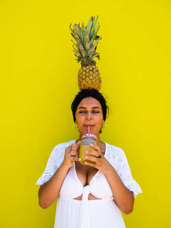 attractive Brazilian female with pineapple on yellow background. attractive Brazilian female with pineapple and juice on yellow backgroundの写真素材