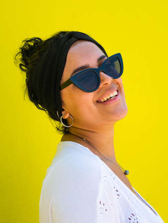 attractive Brazilian female with sunglasses on yellow background. Brazilian female with white dress on yellow backgroundの写真素材