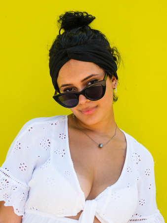 attractive Brazilian female with sunglasses on yellow background. Brazilian female with white dress on yellow backgroundの写真素材