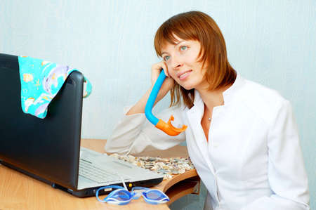 Woman is dreaming about vacation. Diving glasses, swimsuit and seashells in office.の写真素材