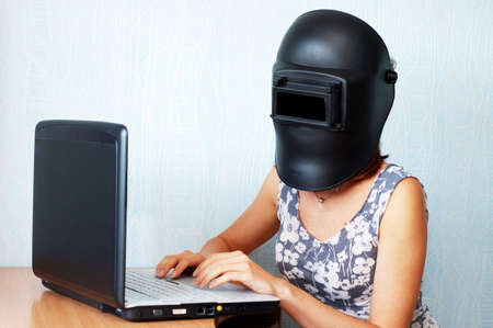 Woman in welding helmet workimg with laptop の写真素材