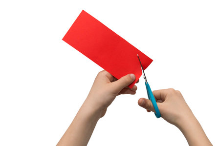 Ð¡hild's hands cutting colored red paper with scissors isolated on white backgroundの写真素材