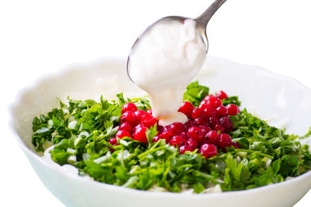 Cooking salad from cutted cabbage, onion, green-stuff and thawed red currant in deep white dish and adding some cream from spoonの写真素材