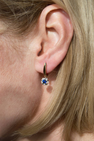 Golden earring with dark blue gem - sapphire and few diamonds in model's earの写真素材