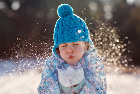 Adorable young girl blowing snowflakes into fresh winter airの写真素材