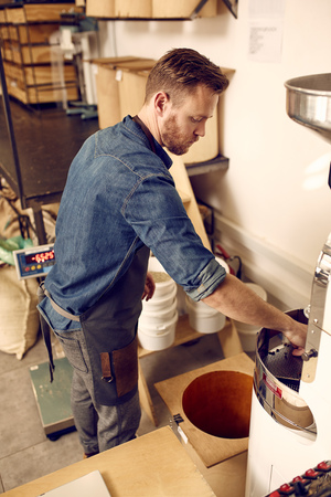 Hipster man in a modern coffee roastery working with a modern roasting machine in a neat and organised coffee distribution spaceの写真素材