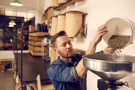 Male entrepreneur in his coffee roastery and distribution space preparing a new batch of roasted...