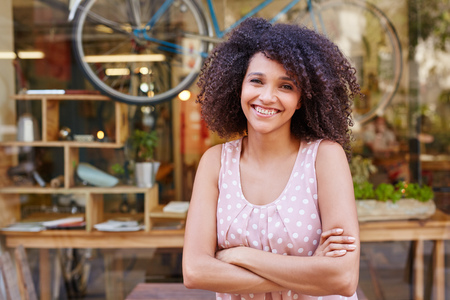 Beautiful mixed race woman standing confidently outside the front of her coffee shopの写真素材