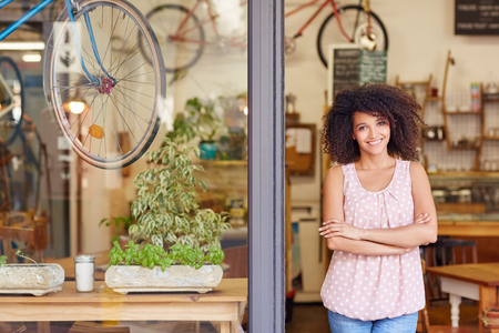 Young mixed race woman smiling, while standing in the door of her cafe with her arms folded proud to be the owner of a small businessの写真素材