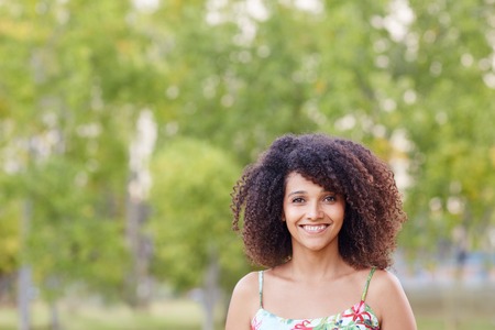 A young woman standing a park with trees behind herの写真素材