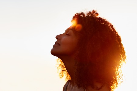 Profile protrait of a beautiful woman with afro style hair silhouetted against golden sun flare on a summer evening Profile protrait of a beautiful woman with afro style hair silhouetted against golden sun flare on a summer evening
