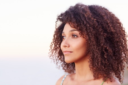 Beautiful mixed race woman with curly afro hair looking serenely away outdoorsの写真素材