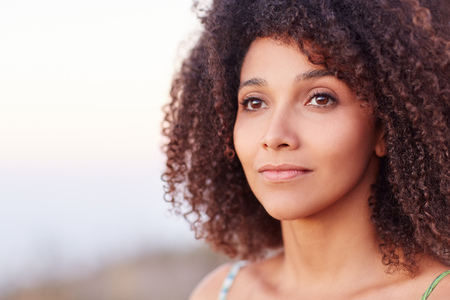 Intimate closeup portrait of a beautiful mixed race woman outdoors looking serenely into the distanceの写真素材
