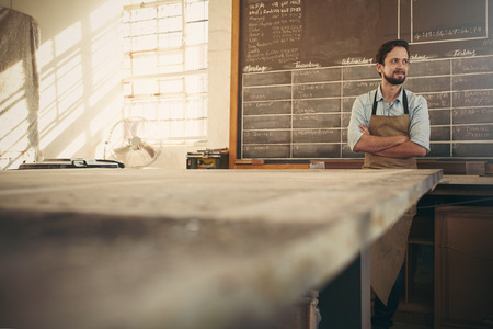 Carpenter craftsman standing with his arms crossed in his workshop with beautiful natural light...